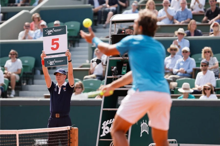 网球比赛现场裁判举牌记分,前景为网球运动员准备发球,背景为观众席